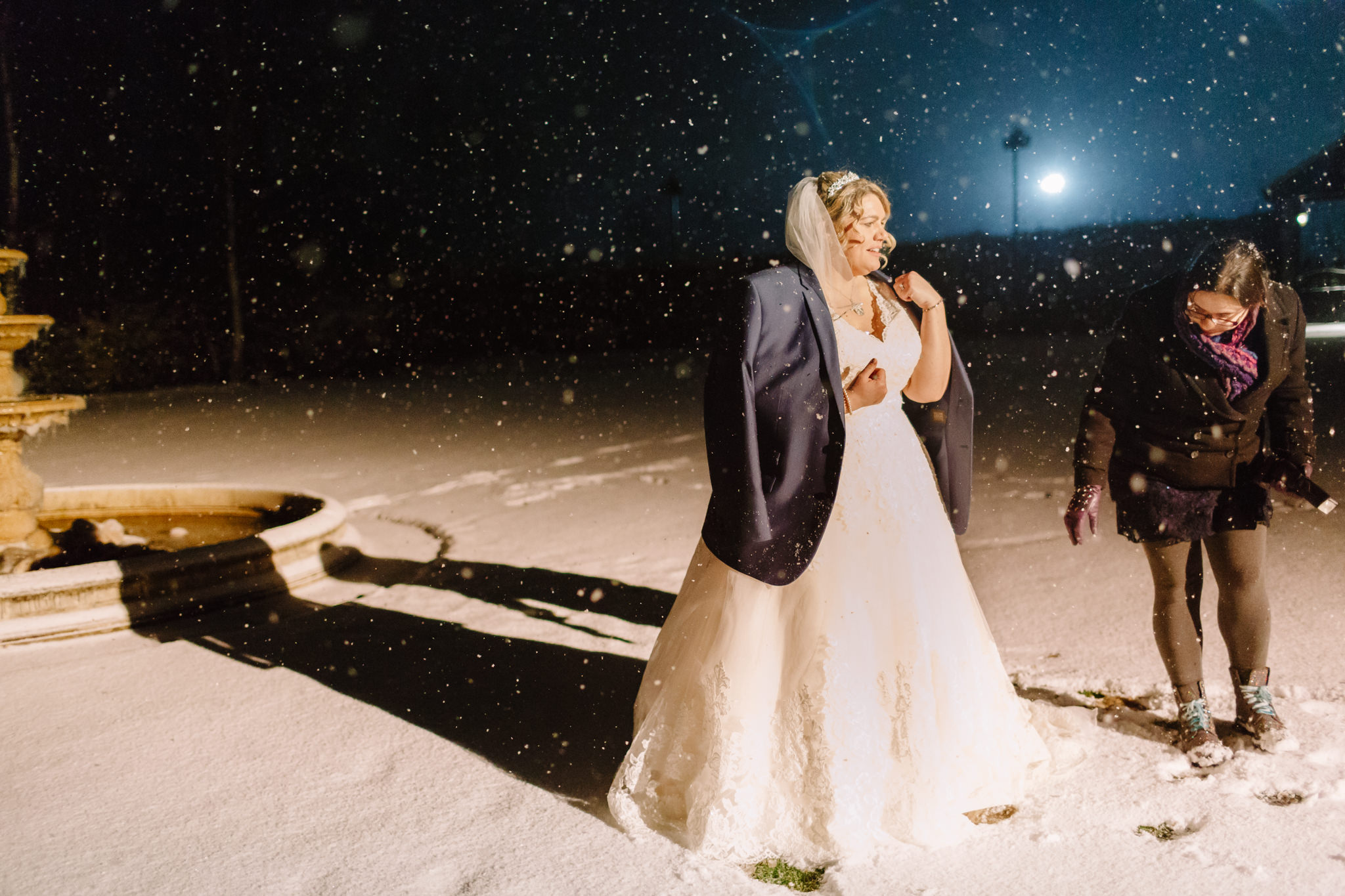 woman helps bride get ready for a shot in the snow