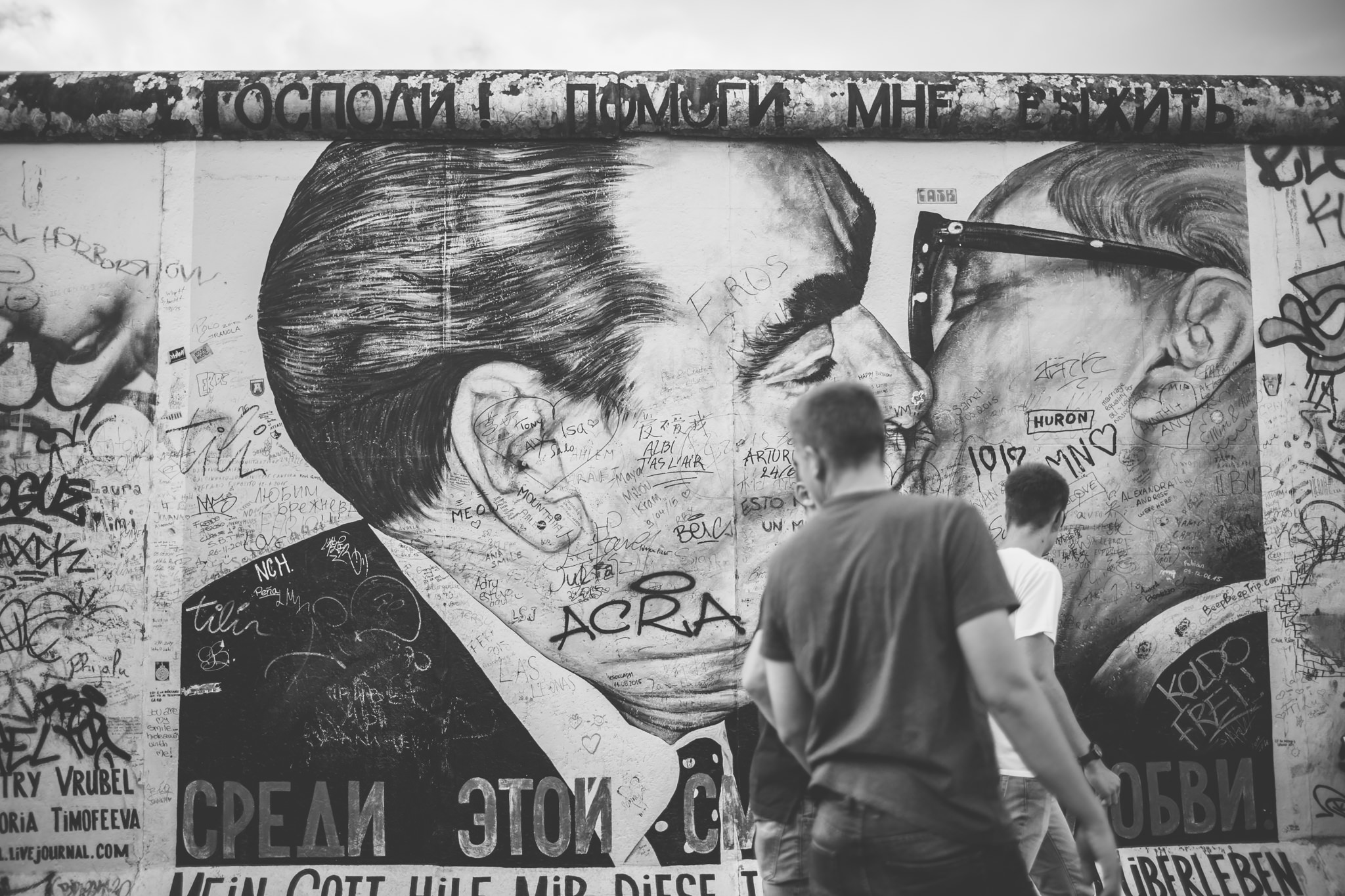 A group of men walks past graffiti on the Berlin Wall