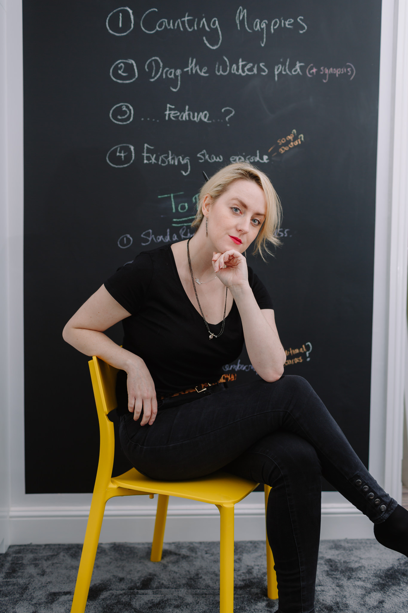 Woman sits in front of chalkboard wall on yellow chair