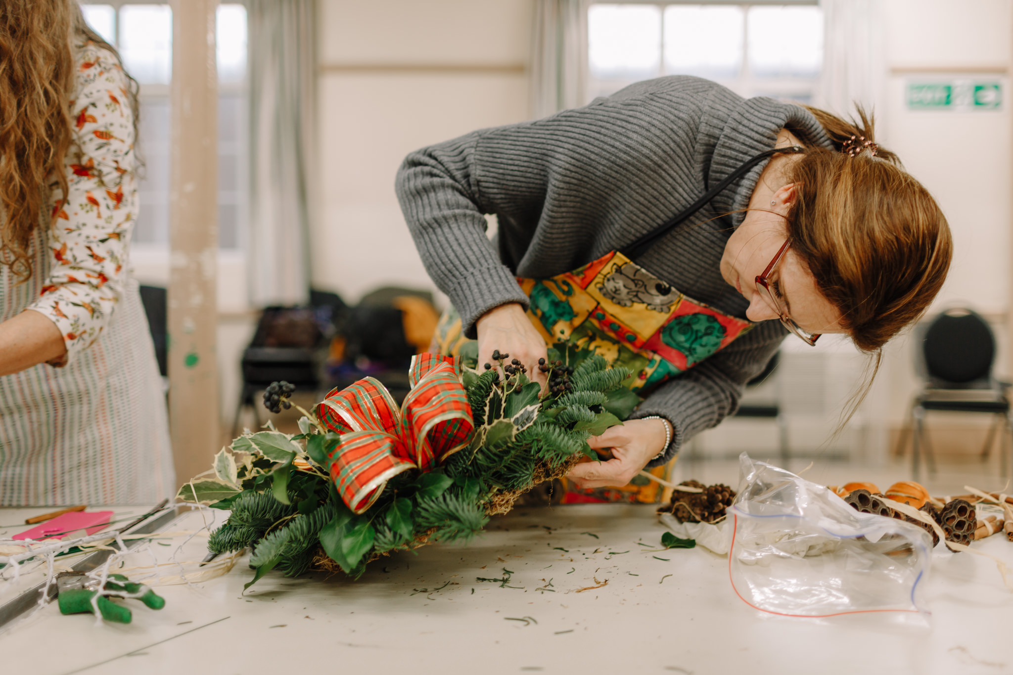 Woman looks closely at her Christmas wreath while attaching decoration to it
